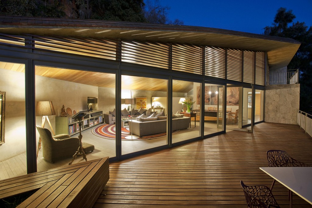 O living é integrado ao deck graças às portas envidraçadas pivotantes. A parede de pedra delimita a cozinha e contrasta com a madeira.