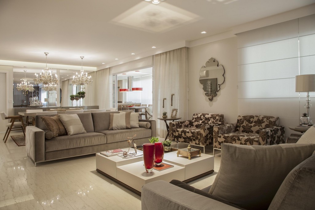 O piso de porcelanato e o teto rebaixado de gesso dão unidade à área social, que é separada pela disposição dos móveis e a iluminação, planejada em pontos de luz. Os sofás e as poltronas receberam veludo cristal liso e estampado. As persianas em estilo romano e as cortinas voal filtram a luz natural com estilo. Foto por J. Vilhora