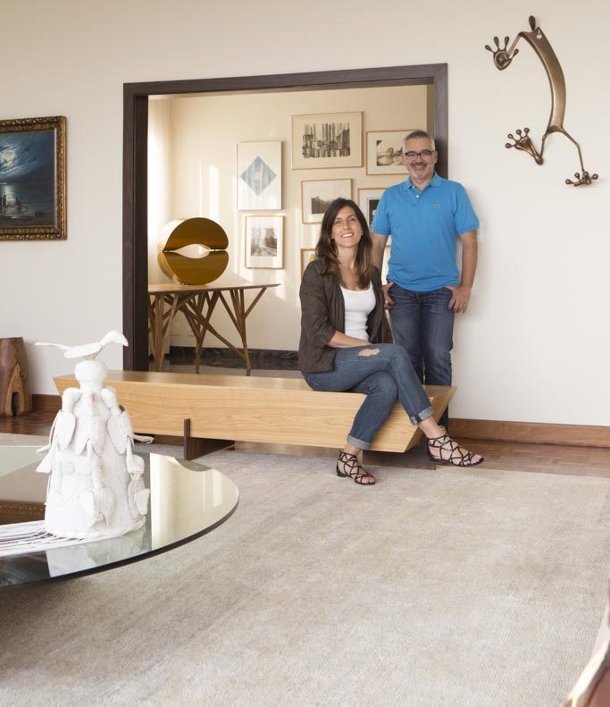 Daniela e Ricardo posam em frente a uma composição de quadros na casa dos pais da designer, onde o lifestyle e desejos dos clientes reflete muito o estilo do próprio escritório. O gosto do casal por acabamentos naturais, como palhinha e madeira freijó, é o mesmo preferido pelos profissionais do Díptico.