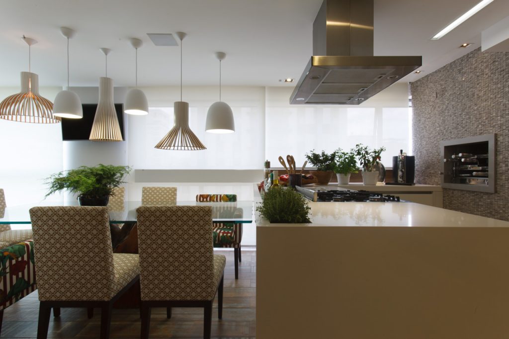 A área gourmet, uma grande prioridade da proprietária que adora promover jantares, foi equipada para receber: ganhou churrasqueira, coifa, fogão, TV e a grande bancada de quartzo branco que se acopla à mesa de vidro. Para trazer mais aconchego, o piso de porcelanato simula madeira de demolição. 