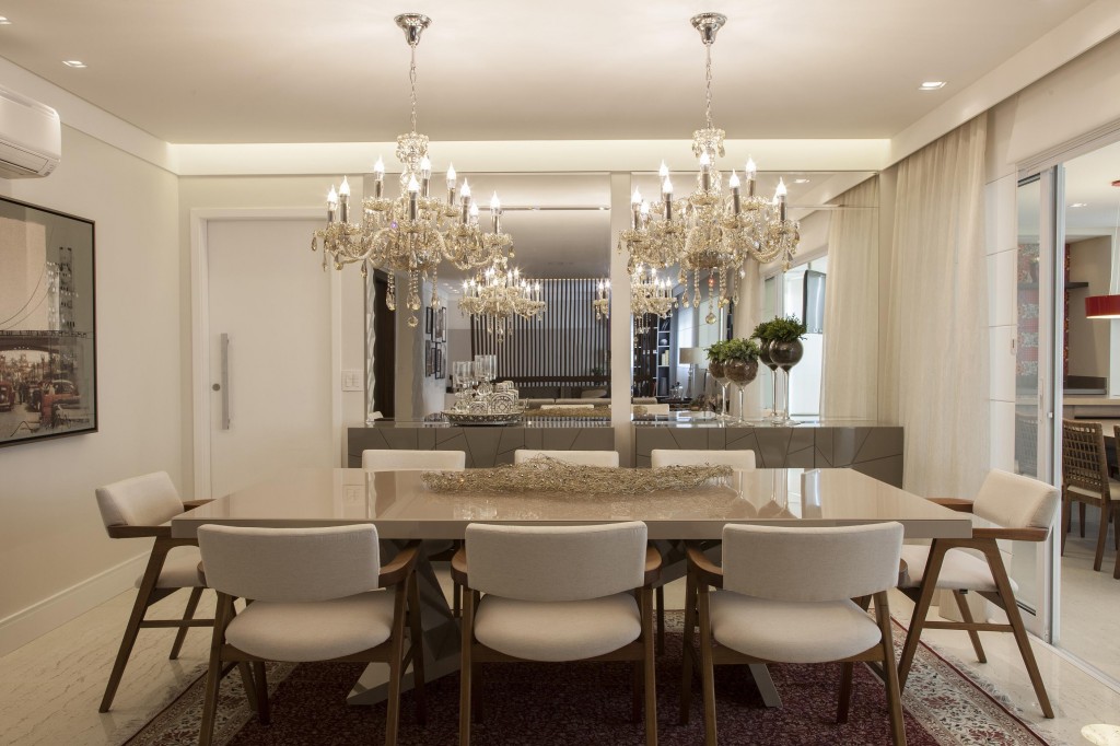 A sala de jantar é definida pelos lustres de cristal sobre a mesa de jantar laqueada acompanhada de cadeiras com design anos de 1950, da A Especialista. Ao fundo, dois bufês são encaixados nos nichos espelhados. O tapete é uma recordação de viagem ao Oriente Médio. Foto por J. Vilhora