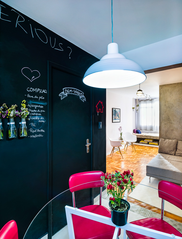 Com a eliminação do quarto de serviços, ganhou-se ainda área para a criação de um estar com sofá e pufe (Oppa). Sobre a parede, aplicou-se cimento queimado como estratégia para camuflar a viga, que também ganhou o mesmo tratamento e destacar a porta de acesso à suíte. Na cozinha, a parede principal recebeu tinta preta fosca, formando uma lousa para recados.