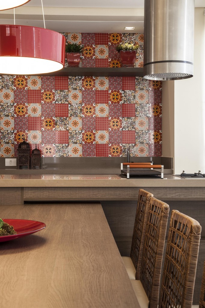 Os ladrilhos hidráulicos com estampas florais em tons de vermelho predominam a área externa. A cor quente também está presente nas luminárias da Bela Luz. A churrasqueira leva design e garante praticidade ao preparo de alimentos sobre bancada em forma de ilha. Foto por J. Vilhora