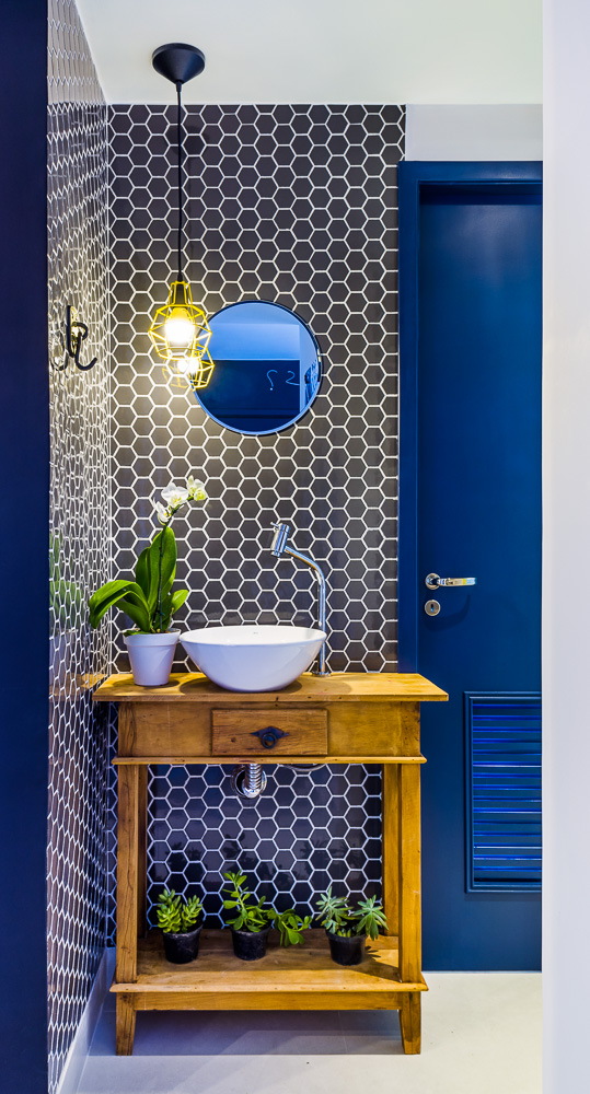 A entrada do lavabo surpreende pela composição das pastilhas Sixties Gray Bold Brilhante (Decortiles), que combina com o azul intenso da porta e o gabinete rústico de madeira.