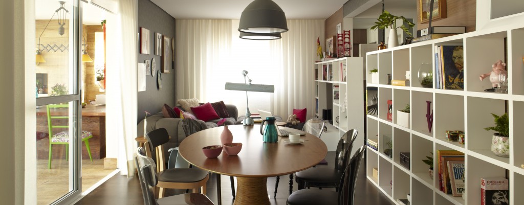 Com a reforma o jantar agora integra-se ao linving. A mesa de madeira com pé torneado é do arquiteto e designer Fernando Jaeger que mistura cadeiras de estilos variados da Micasa. A estante com nichos vazados armazena livros e objetos decorativos e separa o ambiente da galeria. Fartas cortinas da Fina Estampa vedam o espaço quando necessário e protegem da forte incidência de luz solar. As cortinas e persianas são da Fina Estampa.