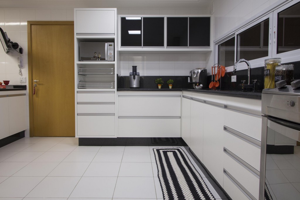 Toda branca, a cozinha é clean e funcional graças à marcenaria acabada em laminado texturizado e vidro que ocupa boa parte das paredes e à farta bancada de trabalho em granito preto, tudo combinando com o piso de porcelanato acetinado e os azulejos entregues pela construtora.