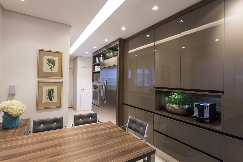 A cozinha, integrada com a sala de almoço, se tornou mais funcional para os moradores. O armário tem portas e gavetões com abertura por toque e nichos para embutir os eletrodomésticos. O projeto luminotécnico mescla pontos de luz próximos à marcenaria e um rasgo com iluminação central (Acerbi).
