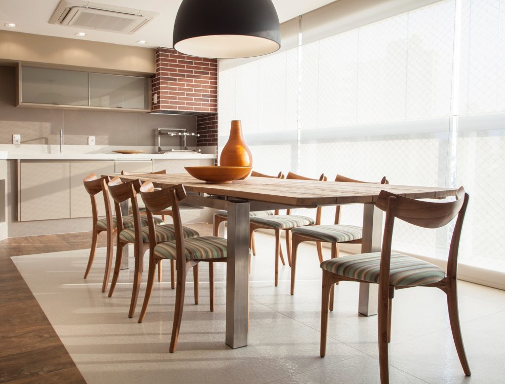 Para o terraço gourmet, a arquiteta instalou armários de apoio (Florense), mesa com tampo de madeira de demolição e pés de metal e cadeiras de espaldar baixo, bem delicadas, acompanhadas de pendente de design moderno (Lustres Iriê).